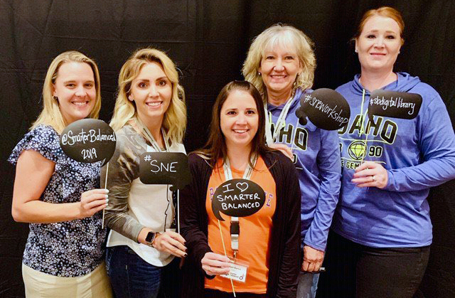 Photo of five educators holding photo booth props that read: @SmarterBalanced 2019, #SNE, I Heart Smarter Balanced, #SNEWorkshop, and #SBDigitallLibrary.
