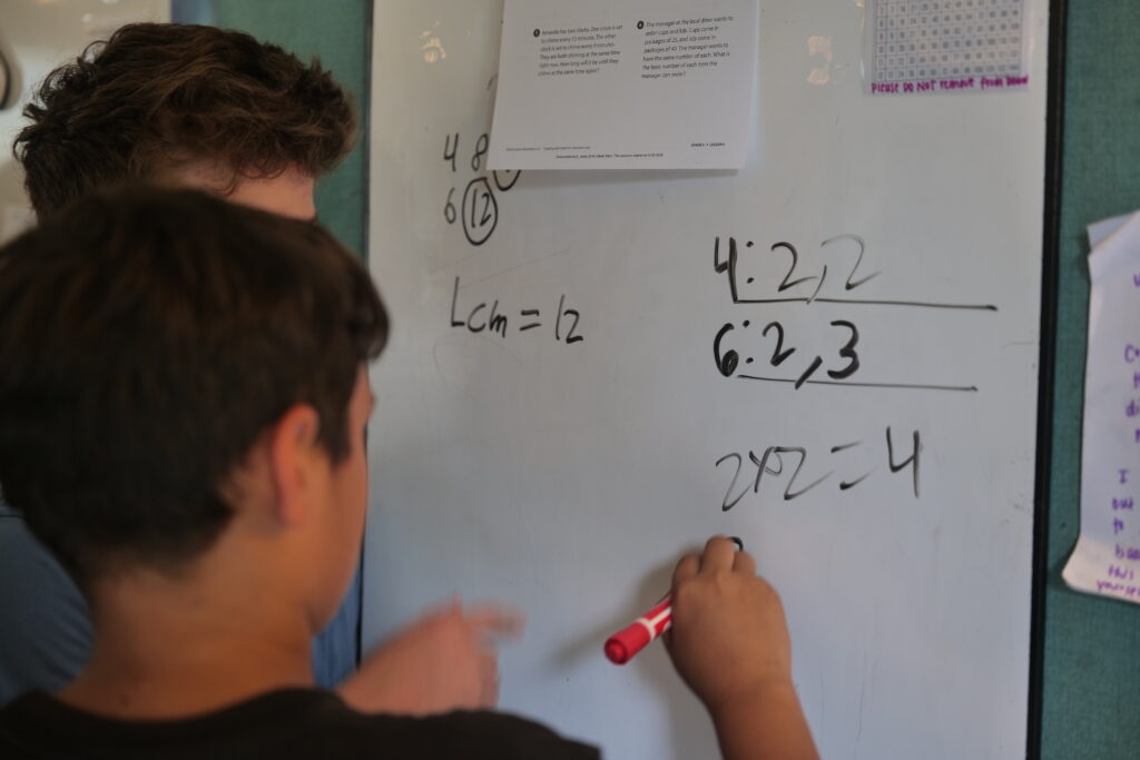 Two students solving math equations at a dry-erase board